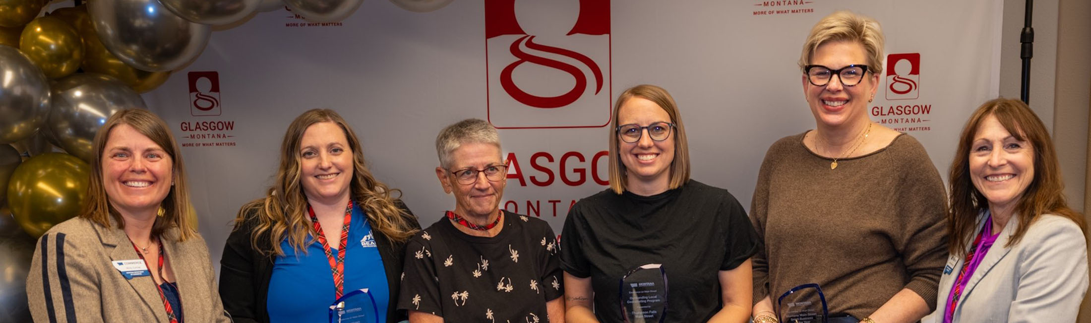 Four awardees were honored in Glasgow today for their downtown revitalization efforts at the first Montana Department of Commerce Excellence on Main Street Awards. (L-R): Commerce Montana Main Street Coordinator Micky Zurcher; Bear Paw Development Corporation Community Planning Director Sara Strissel; City of Boulder Councilwoman Pat Lewis; Thompson Falls Main Street President Kayla Mosher; The Enchanted Room Owner Lisa Kelly; and Commerce Director Marta Bertoglio. Photo credit: Sean R. Heavey.